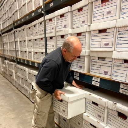 An employee putting a box of documents on a shelf with many other boxes for document storage