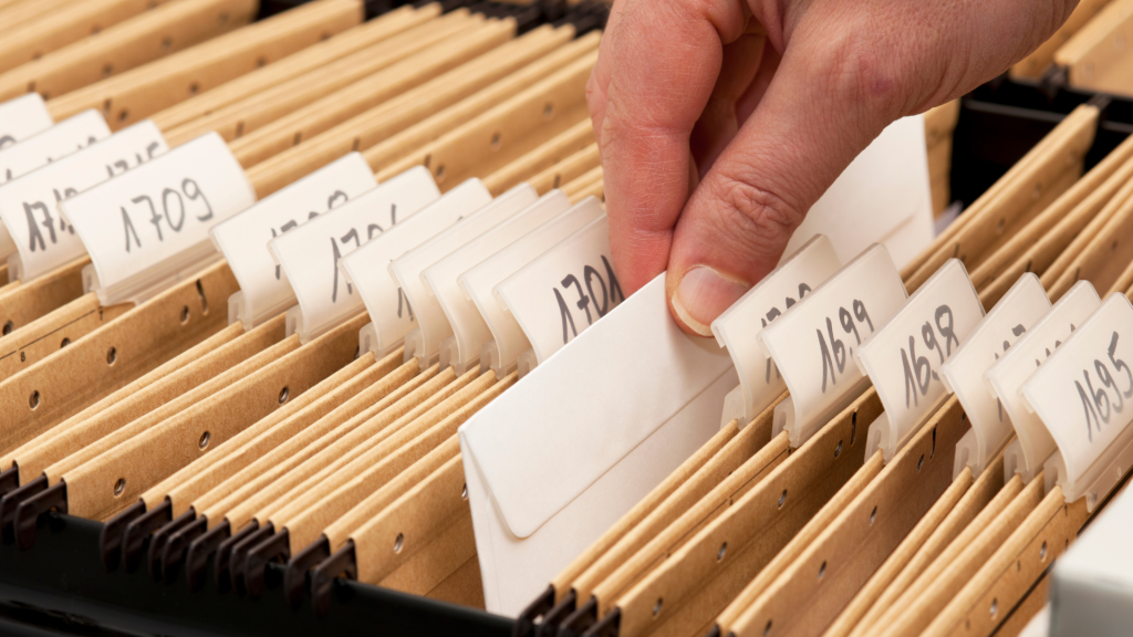 A hand pulling an envelope out of a filing cabinet